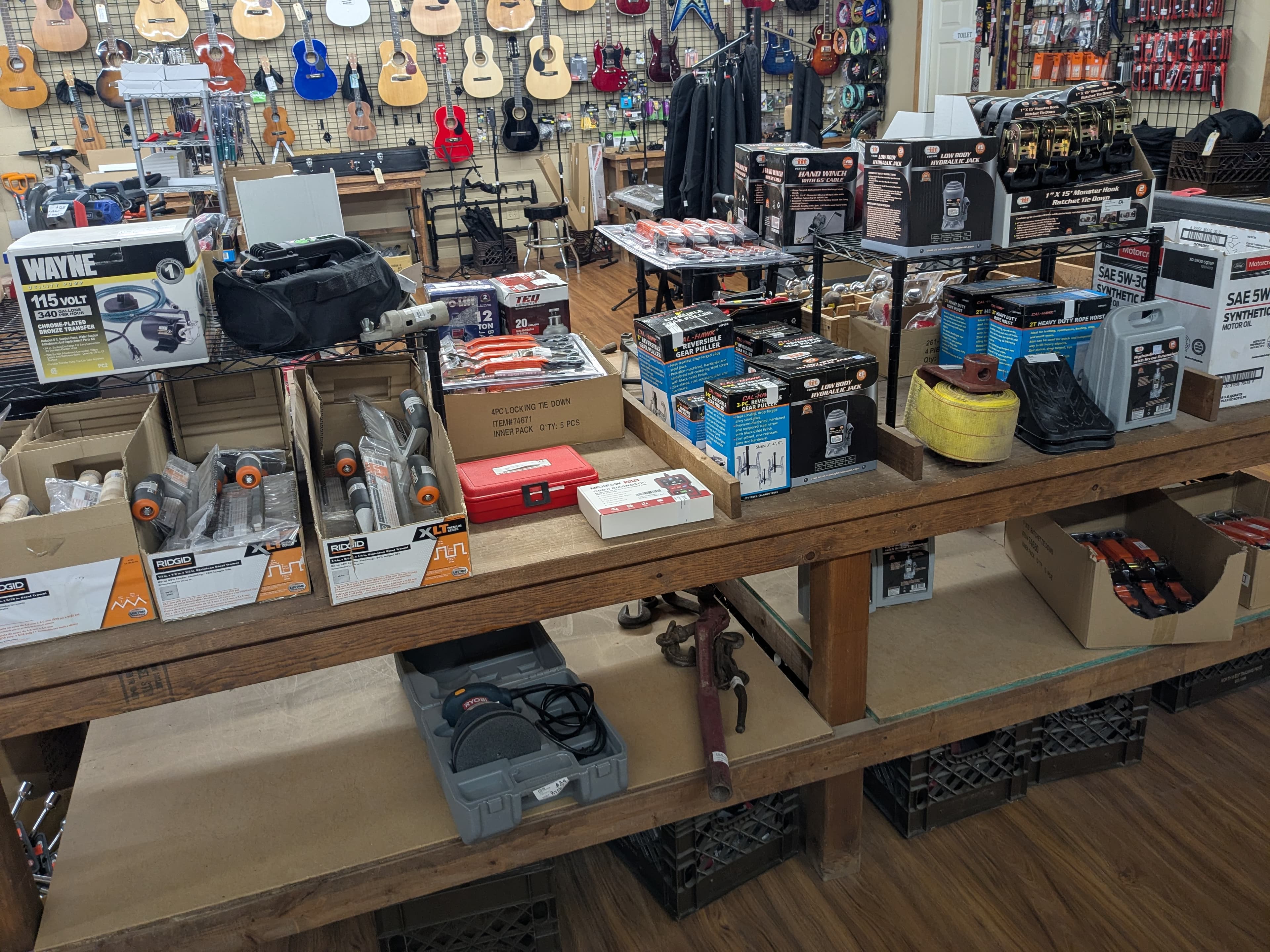 Tools table with Ridgid pipe threaders, hydraulic jacks, and hand winch — acoustic and electric guitars on wall in background