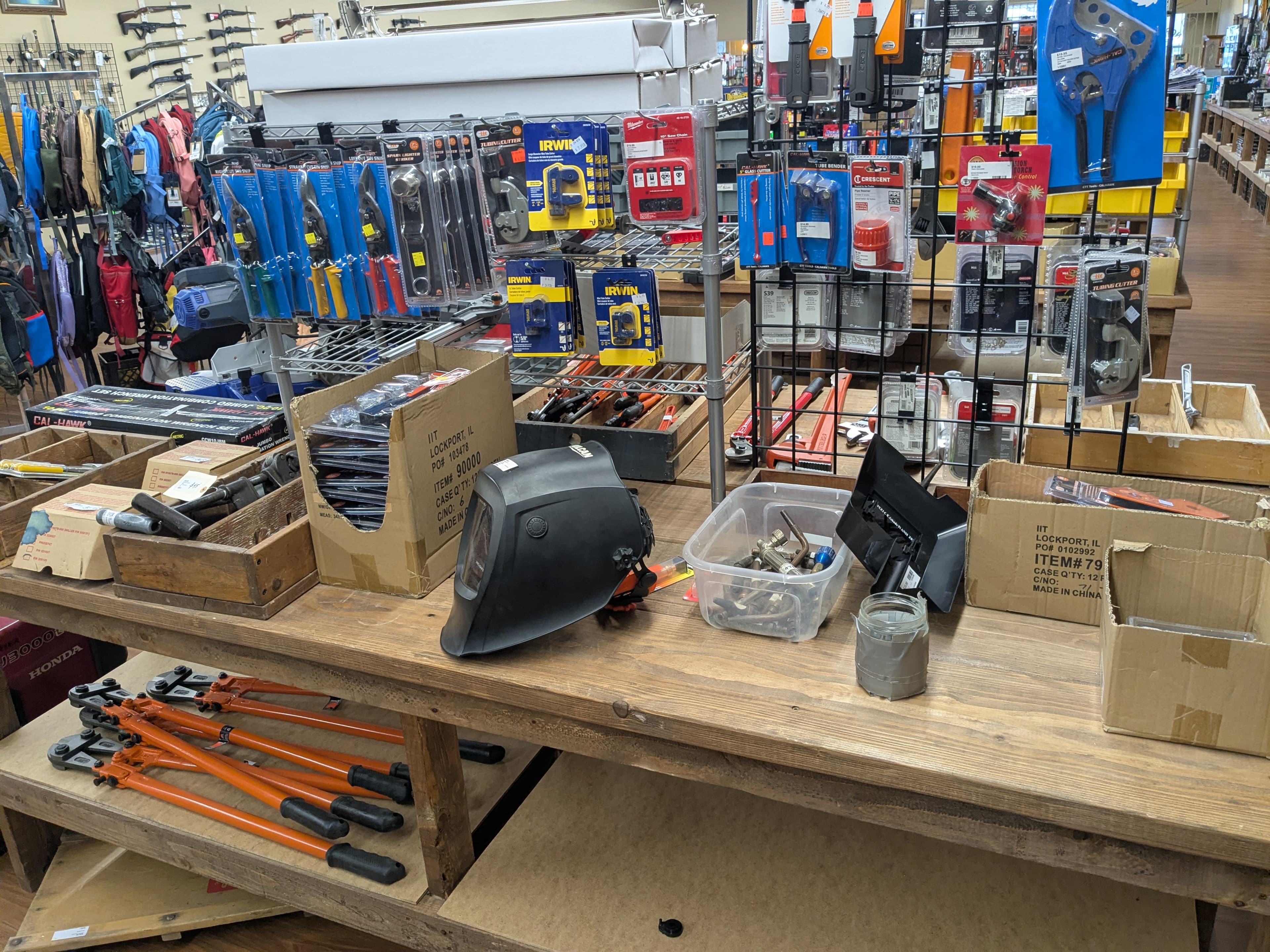Tools table with welding helmet, bolt cutters, and pipe cutters — rifles mounted on wall in background