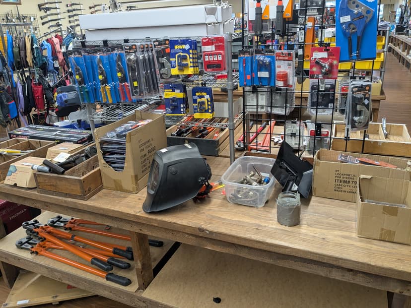 Tools table with welding helmet, bolt cutters, and pipe cutters — rifles mounted on wall in background
