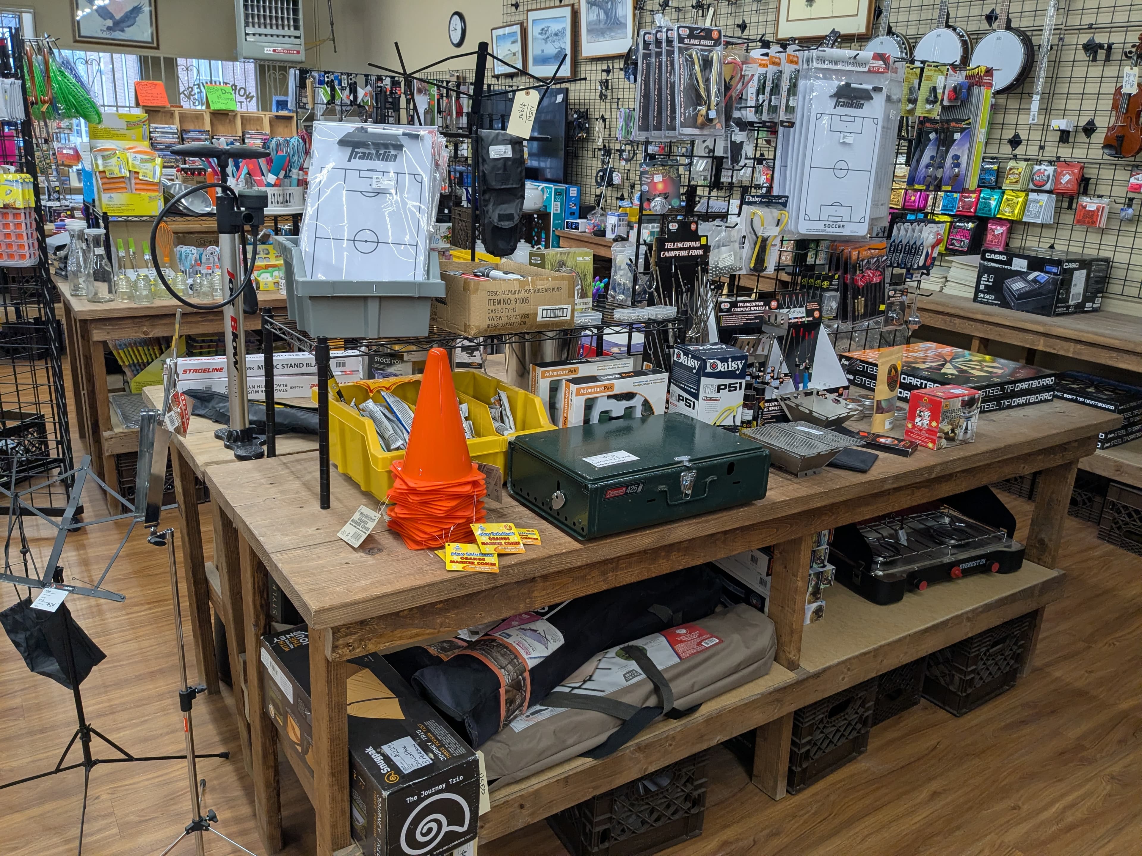Wide store interior showing banjos, keyboards, BB guns, dartboards, music stands, and camping gear