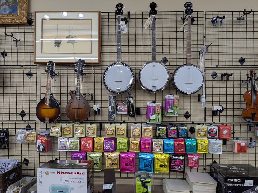Banjos and mandolins on wall, Ernie Ball guitar strings display, KitchenAid mixer, and Casio keyboard