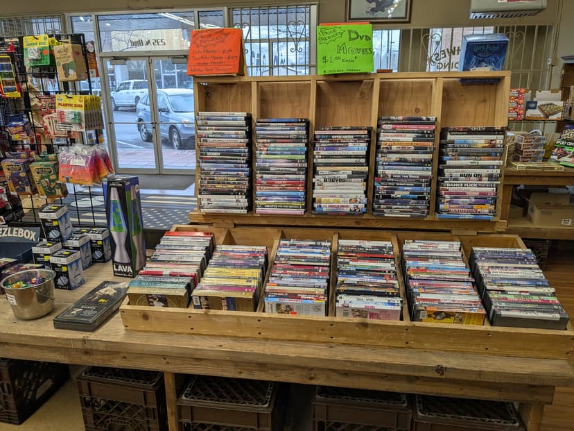DVD and Blu-ray movie shelves with hundreds of titles priced at $1.50 each, plus board games, lava lamp, and novelty items