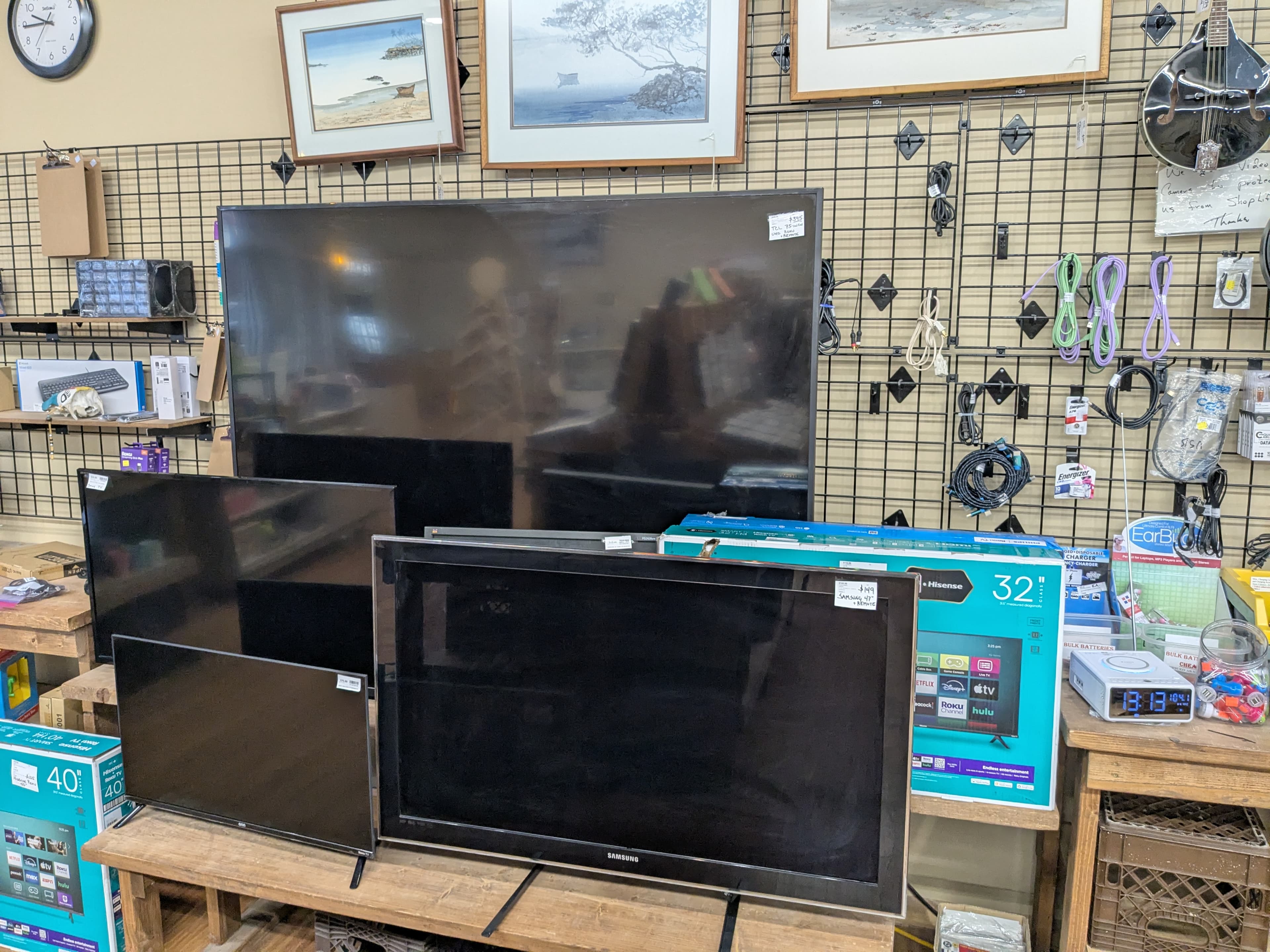 Flat screen TVs in various sizes, framed watercolor art prints, audio cables, and electronics