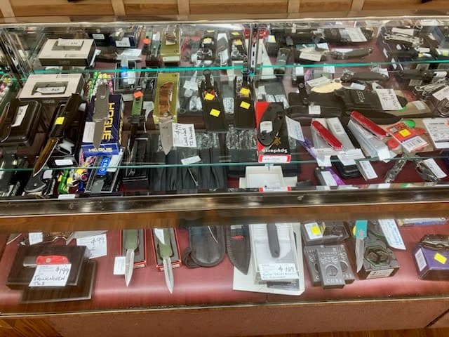 Glass display case with folding knives, tactical knives, and multi-tools from brands like Spyderco and Hogue